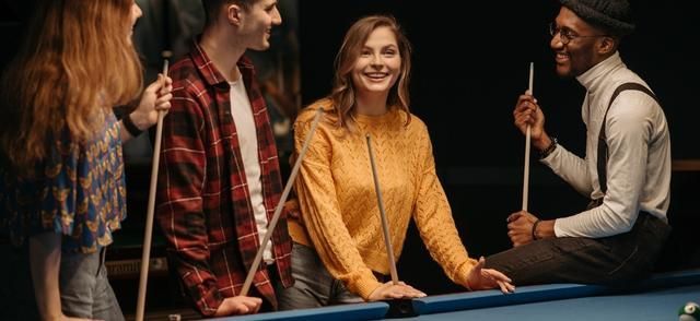 smiling women and men holding cue sticks at a pool table