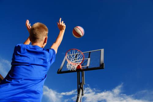 A young boy is throwing a basketball into a basketball hoop.
