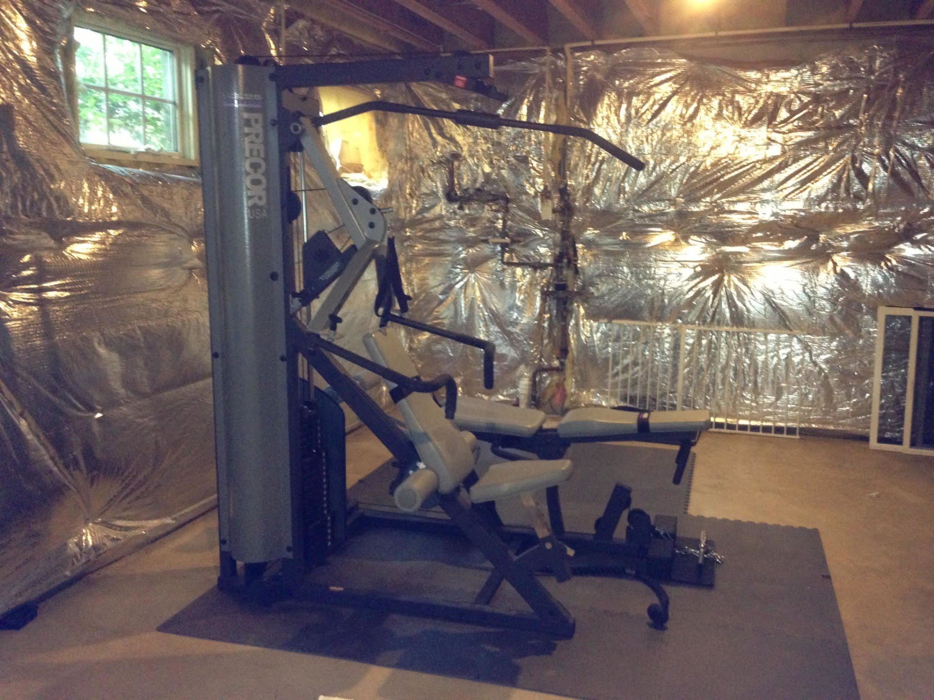 A gym machine is sitting in a basement covered in plastic
