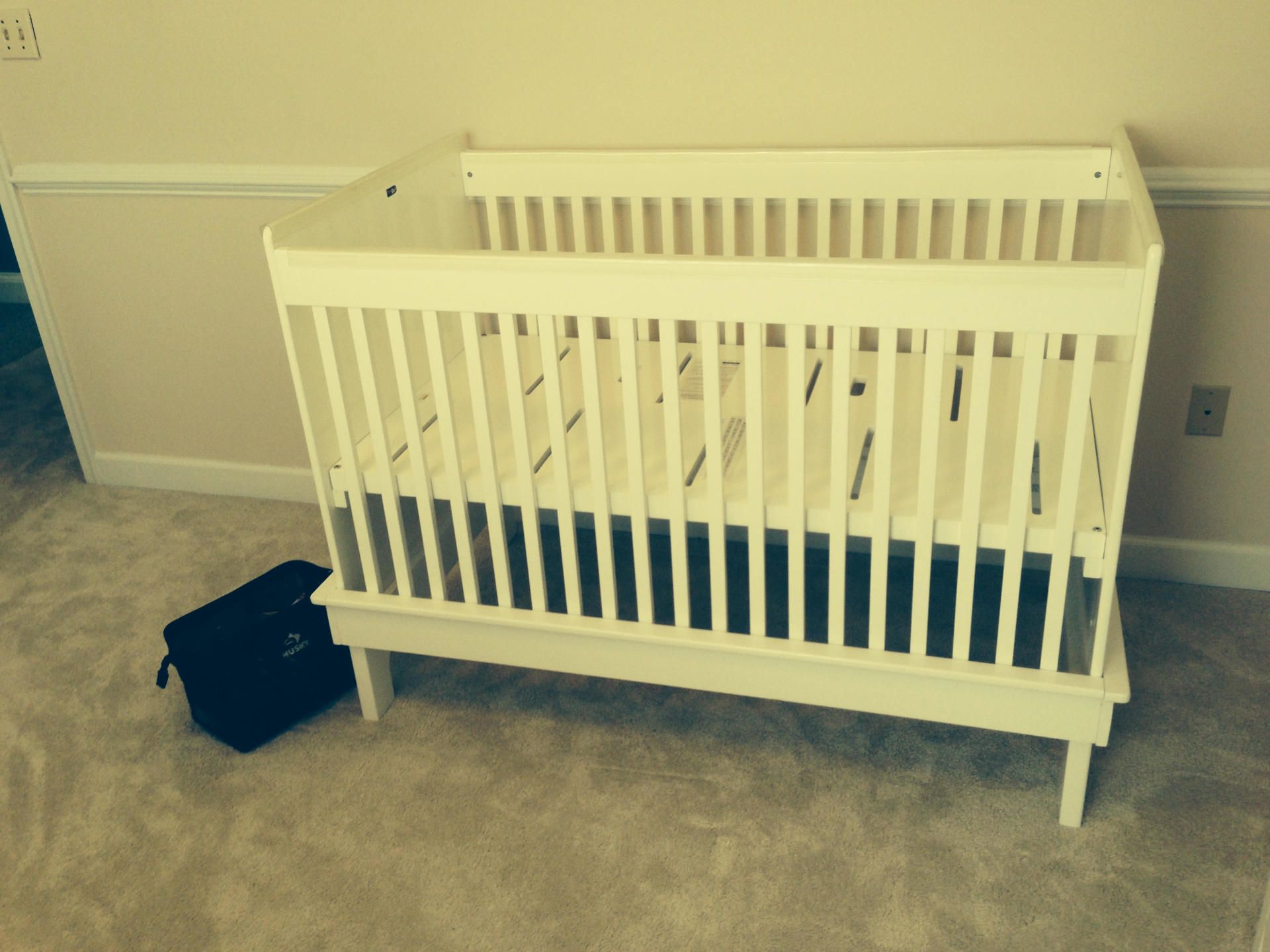 A white crib is sitting in a room next to a black bag
