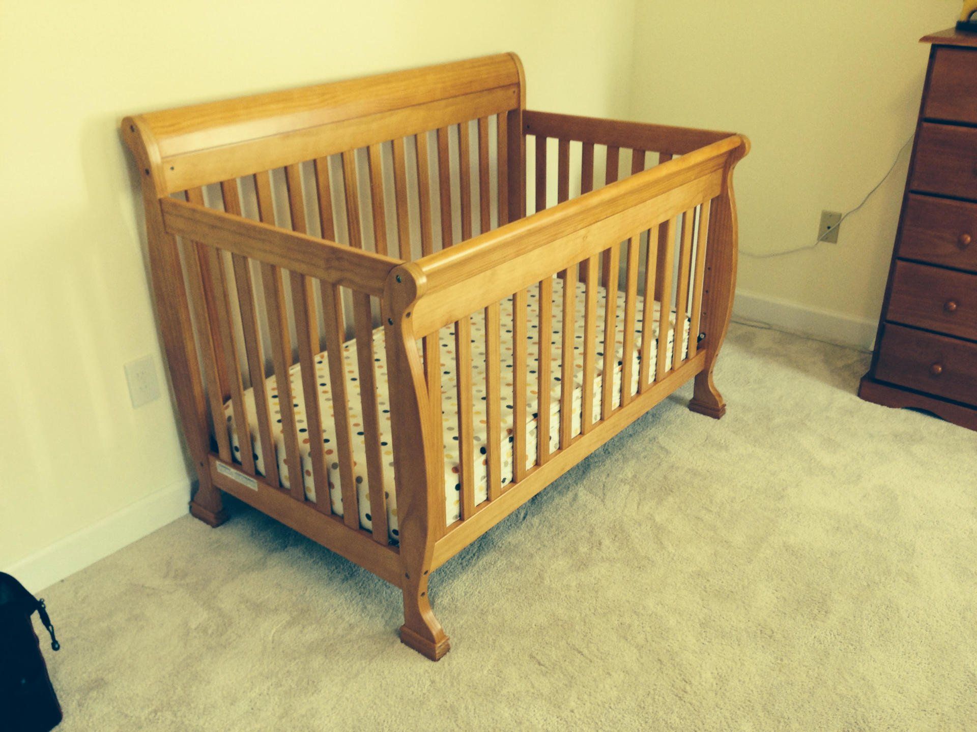 A wooden crib is sitting in a room next to a dresser.