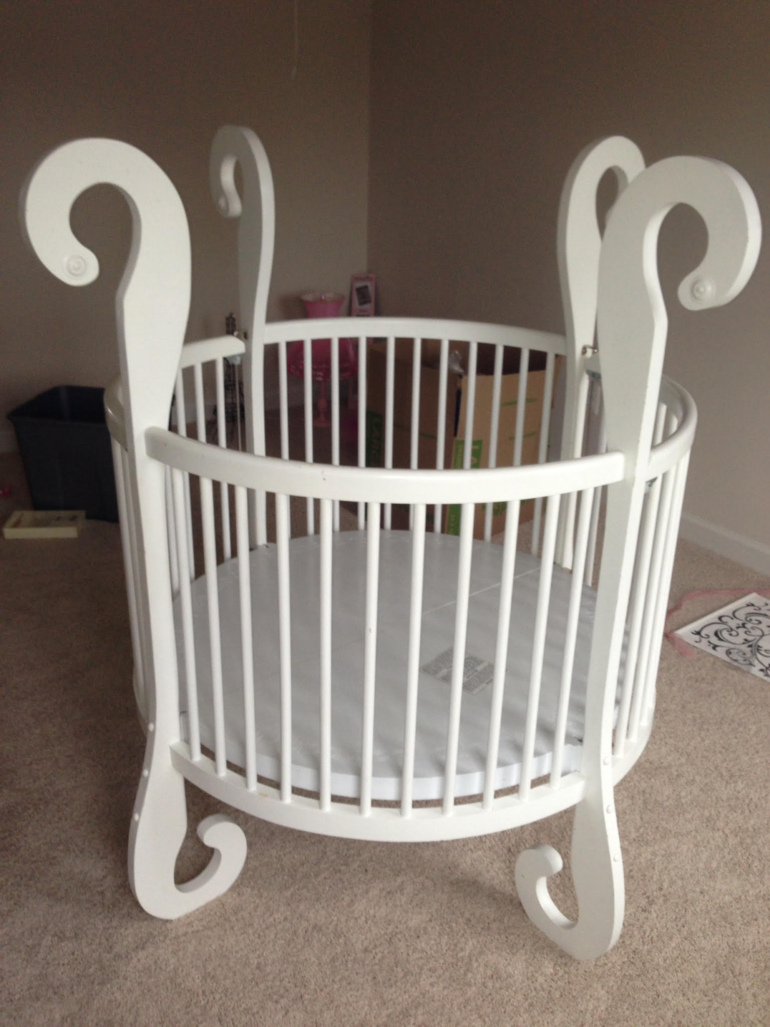 A white round crib is sitting on a carpeted floor in a room.