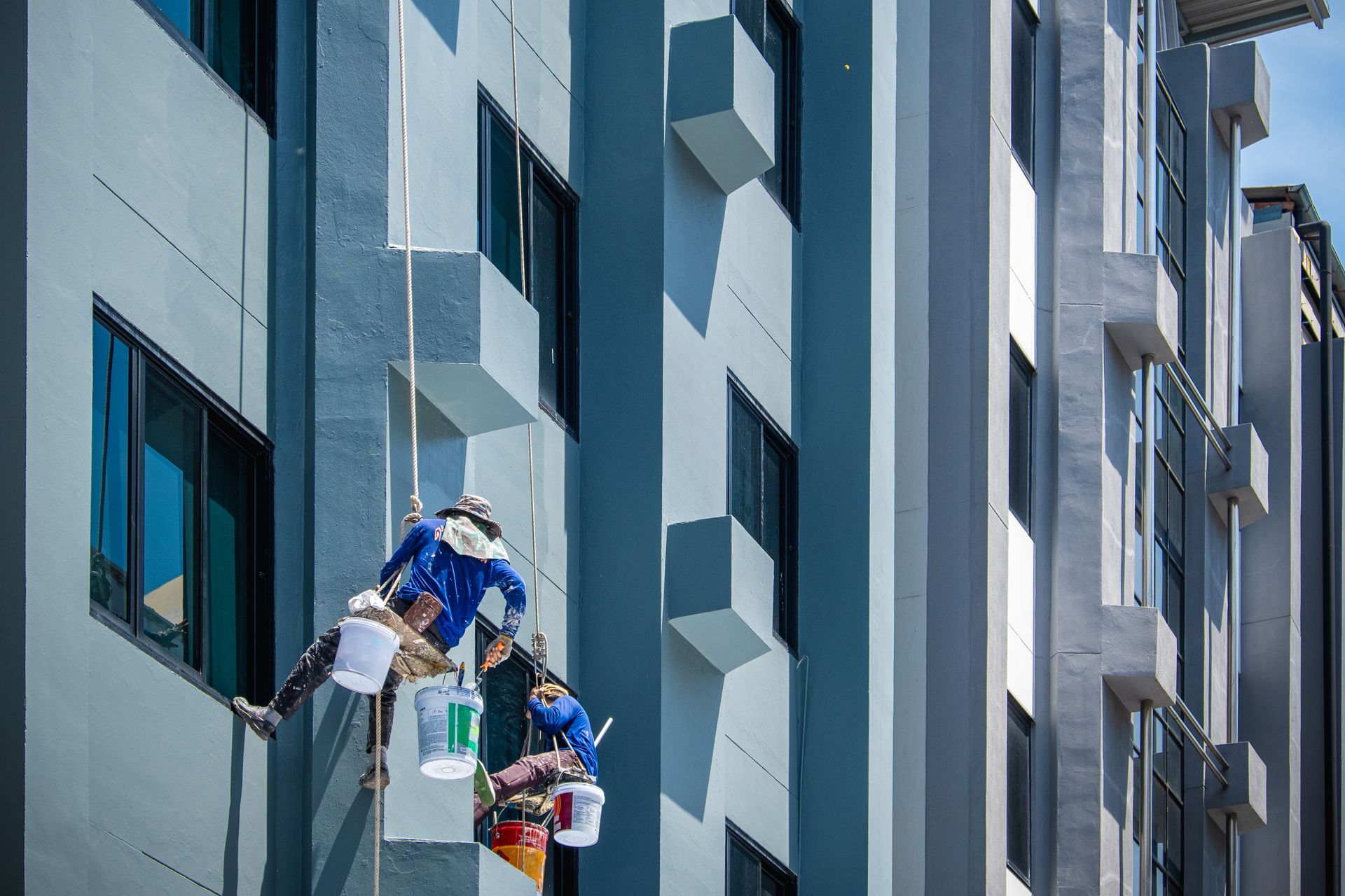 Two window cleaners on ropes working on a tall glass building facade