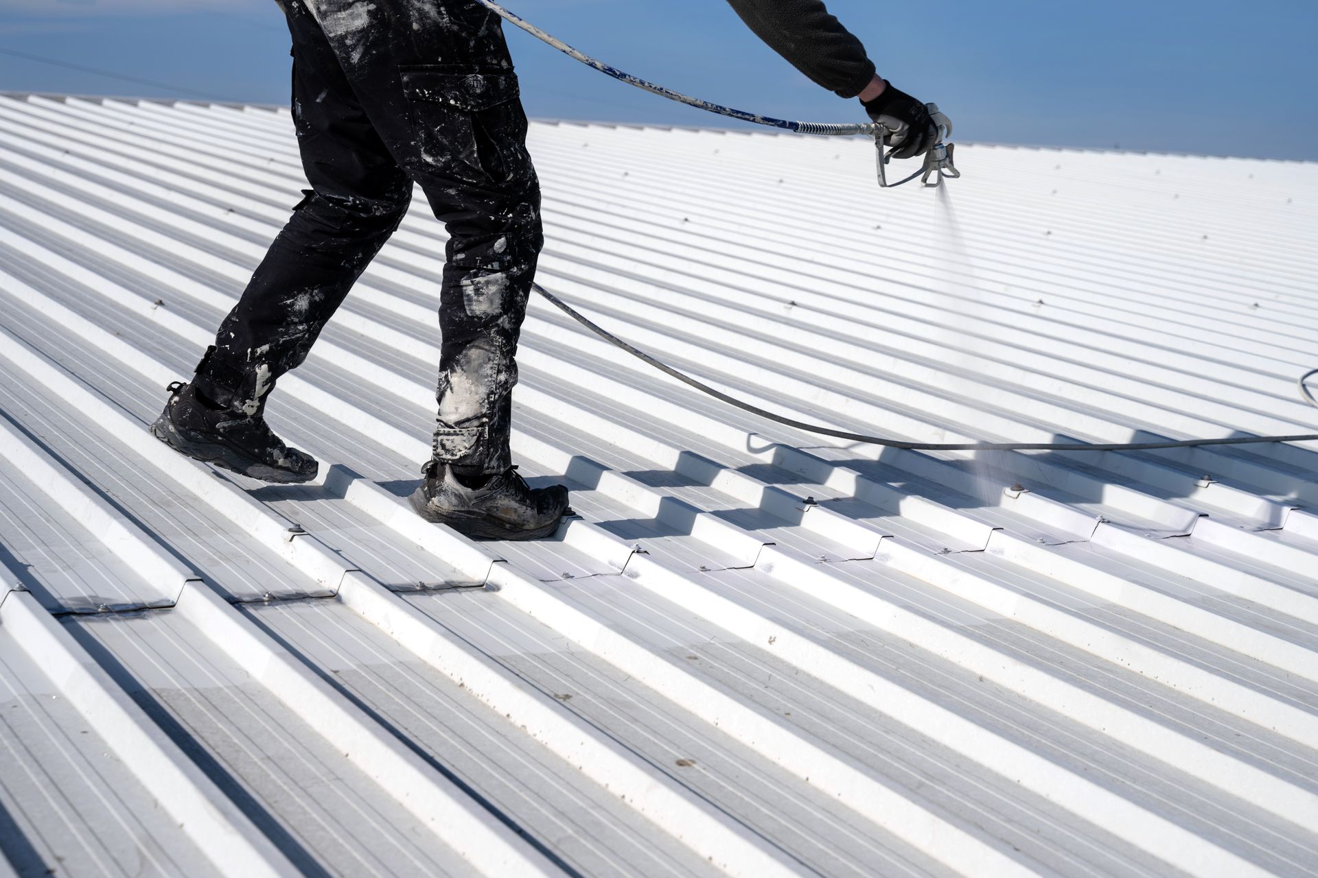 Worker walking on a white corrugated metal roof with a safety harness line Worker walking on a white corrugated metal roof with a safety harness line