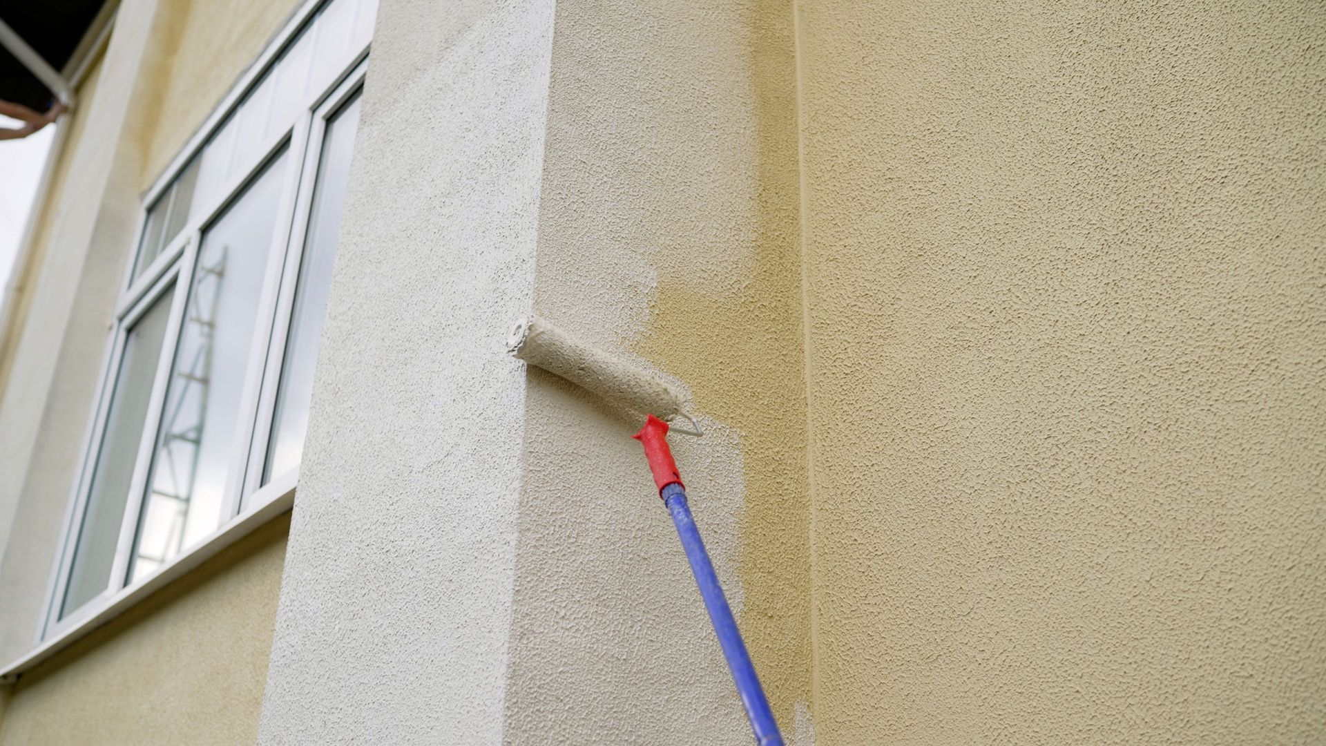 Paint roller applying red paint to a building corner wall next to a window Paint roller applying red paint to a building corner wall next to a window