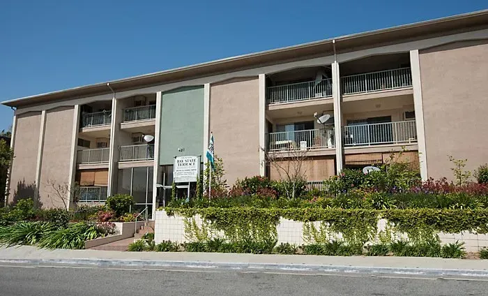 Apartment building with balconies and a landscaped front garden on a sunny day