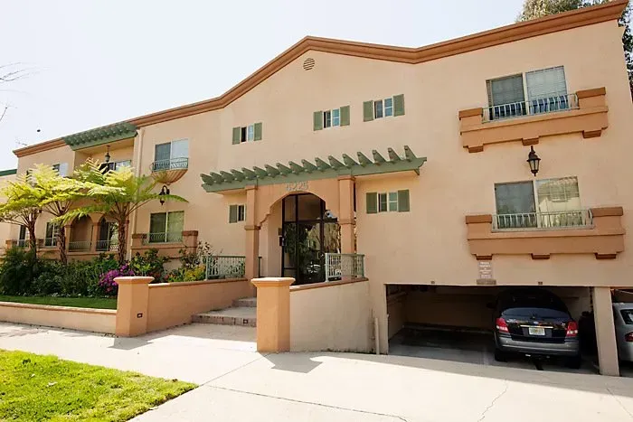 Two-story beige townhouse with green awnings, a front entrance, and a car parked in the garage.