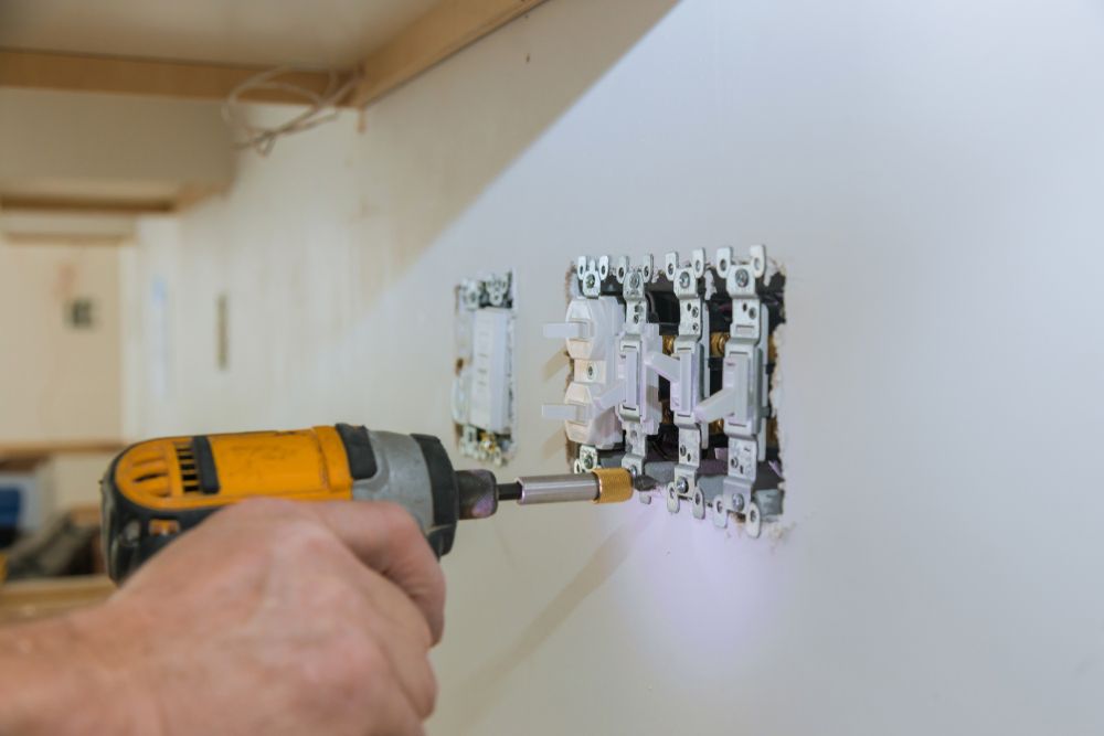 A person is using a drill to install a light switch on a wall.