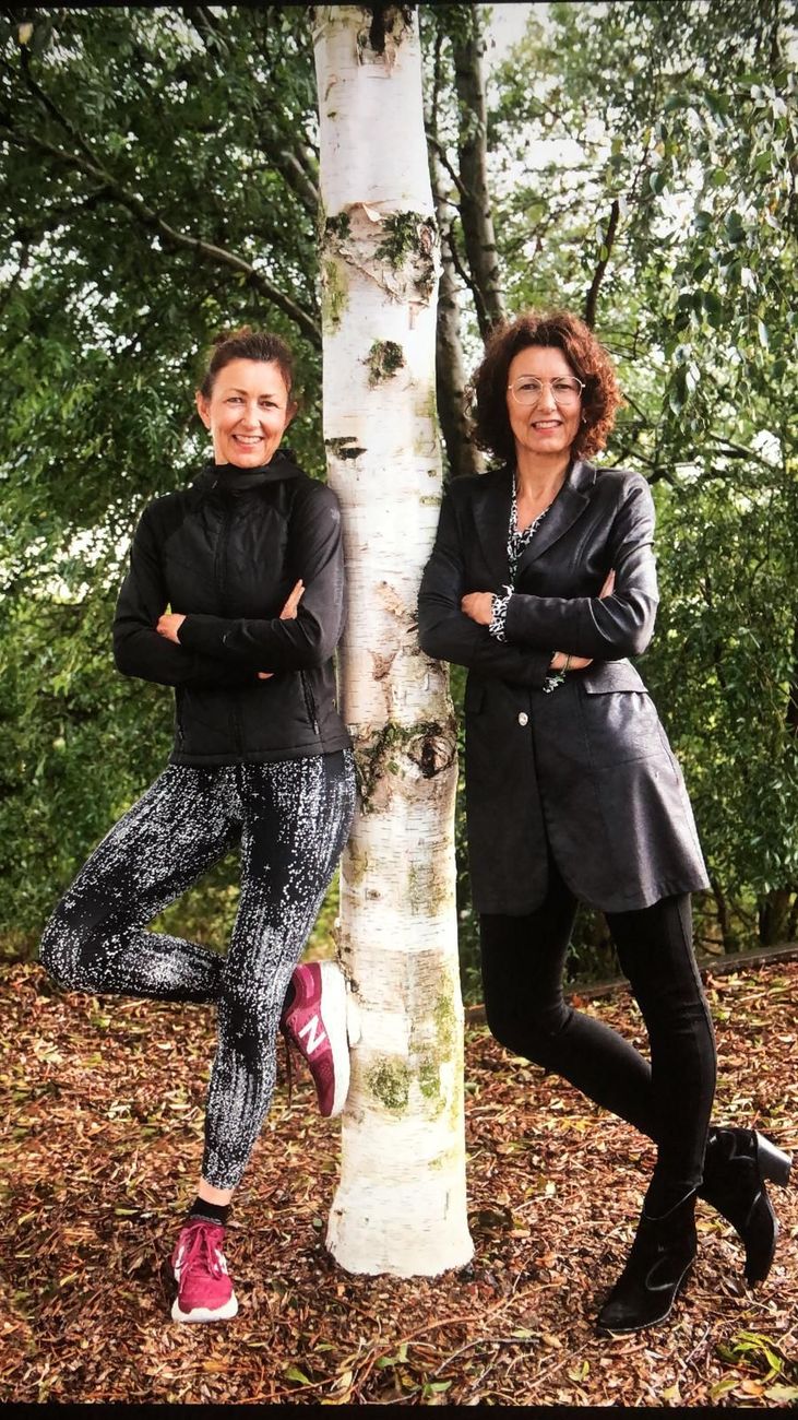 Twee mensen staan ​​met gekruiste armen tegen een berkenboom in een bosrijk gebied, glimlachend.