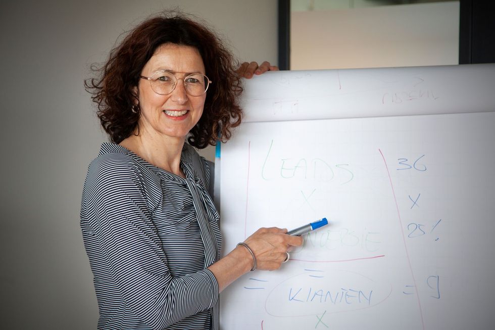 Vrouw wijst met een stift naar een whiteboard in een klaslokaal of kantoor.