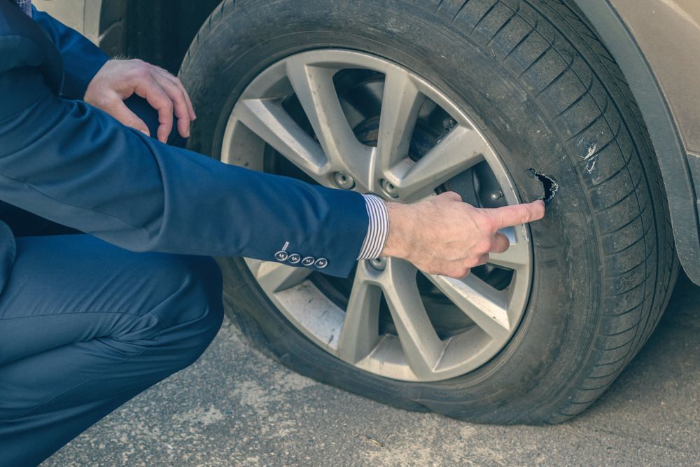 A Man In A Suit Is Pointing At A Flat Tire On A Car — Tyre Master Albury In Wodonga, VIC