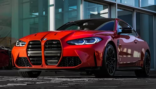 Red sports sedan parked outside a modern building, front view with black rims and grille.