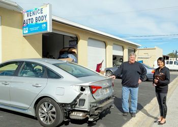 a man and a woman are standing in front of a venice auto body shop .