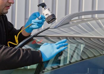 a man wearing blue gloves is fixing a windshield on a car .