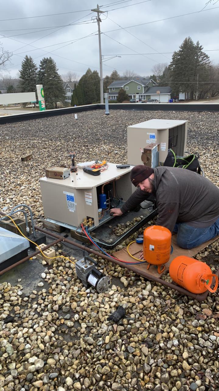 A man is working on an air conditioner on a roof.