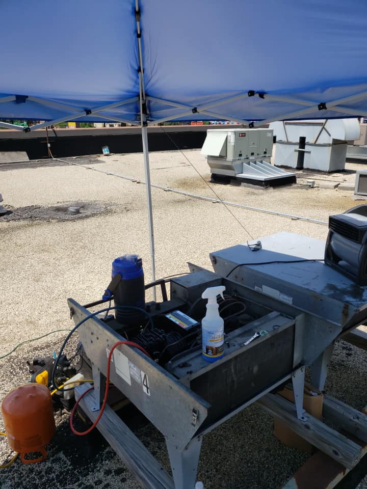 A machine is sitting under a blue tent on a roof.