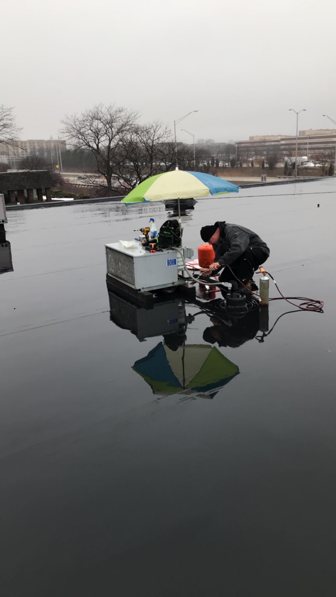 A man is fishing in a lake with an umbrella.