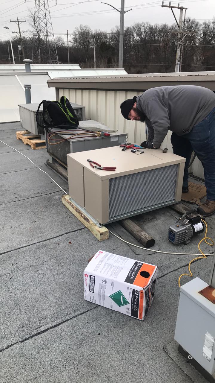 A man is working on an air conditioner on the roof of a building.