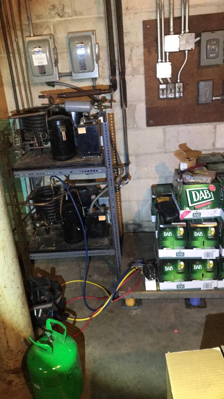 A green gas cylinder is sitting in a garage next to a stack of beer boxes.