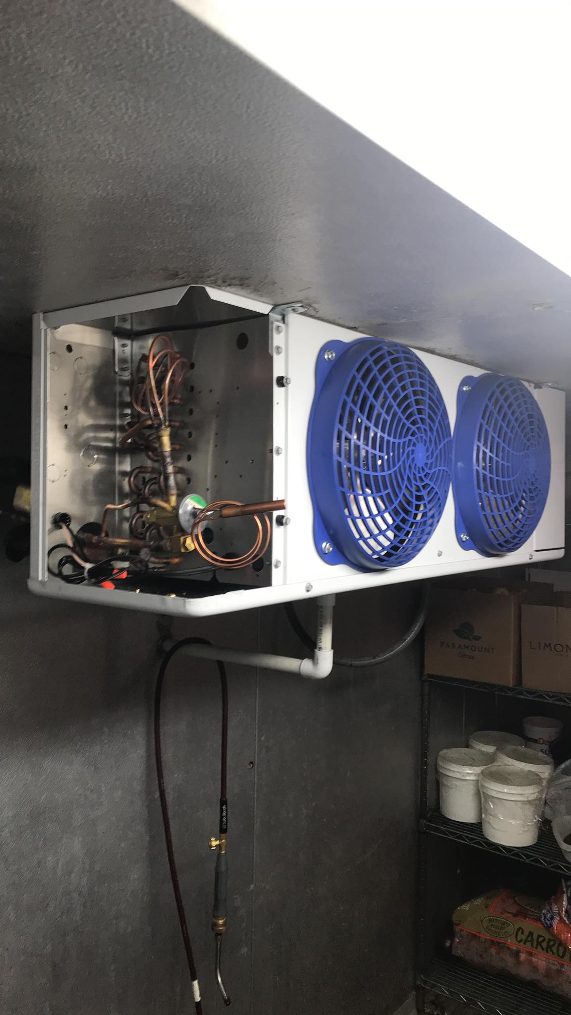 A refrigerator with two blue fans hanging from the ceiling.