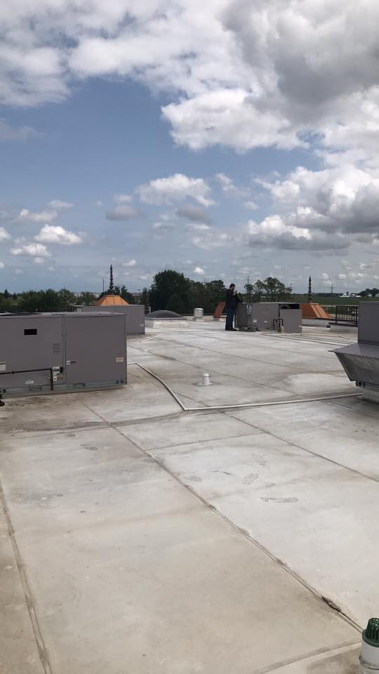 A man is standing on top of a roof with a blue sky in the background.