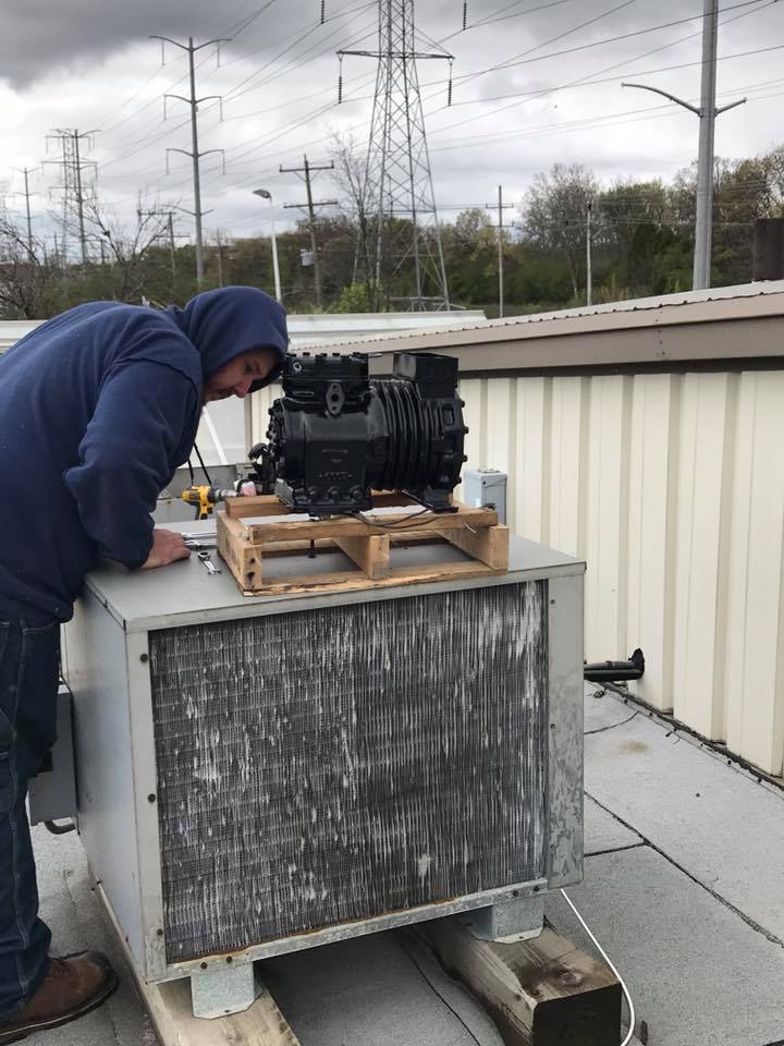 A man is working on an air conditioner on the roof of a building.