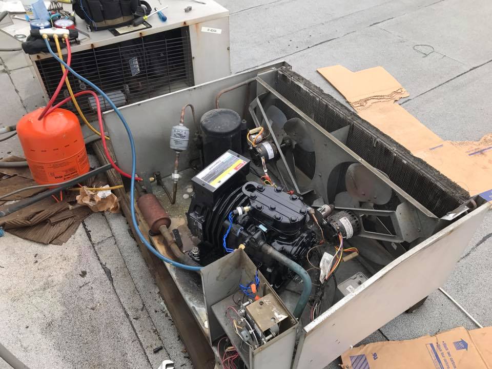 An air conditioner is being repaired on the roof of a building.
