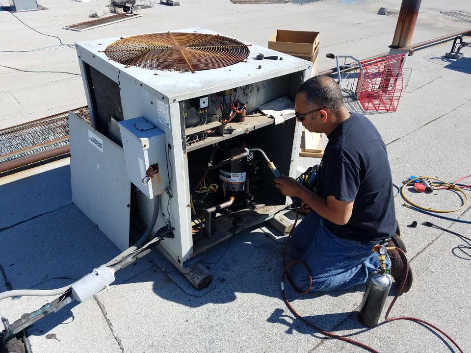 A man is working on an air conditioner on a roof