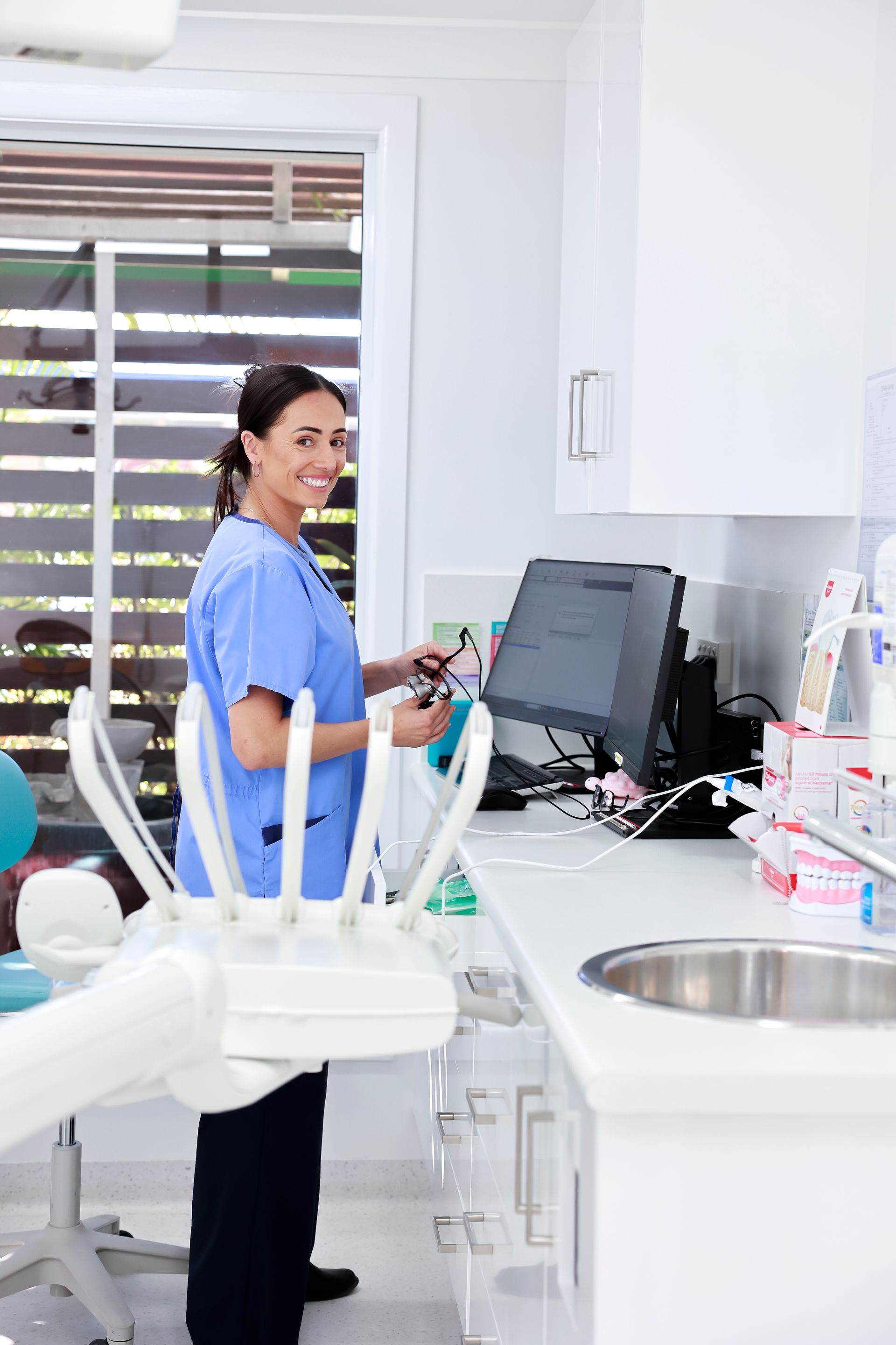 Dentist in blue scrubs smiles while using a computer in a bright dental office - O'Reilly Dental