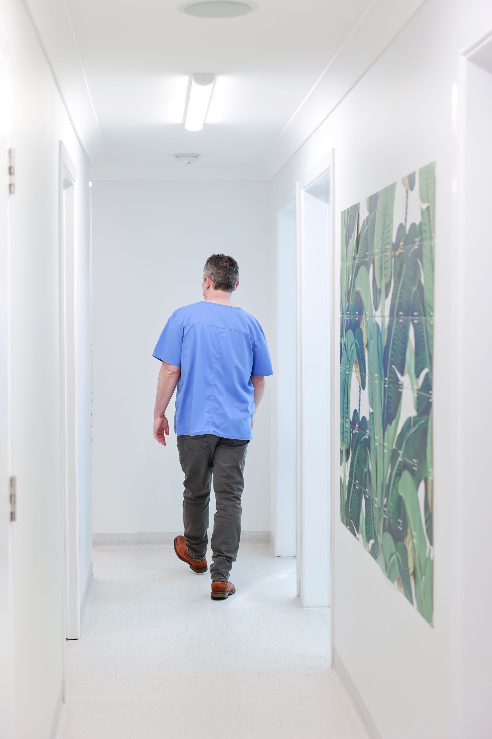 Person in blue scrubs walks down white hallway toward a bright light - Reception area O'Reilly Dental