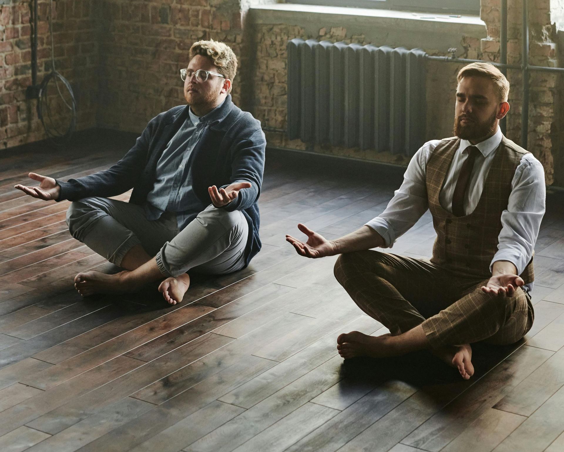 Two men are sitting on the floor in a lotus position.