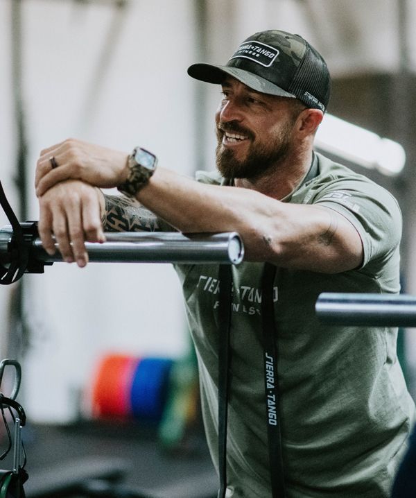 A man wearing a hat is leaning on a barbell in a gym.