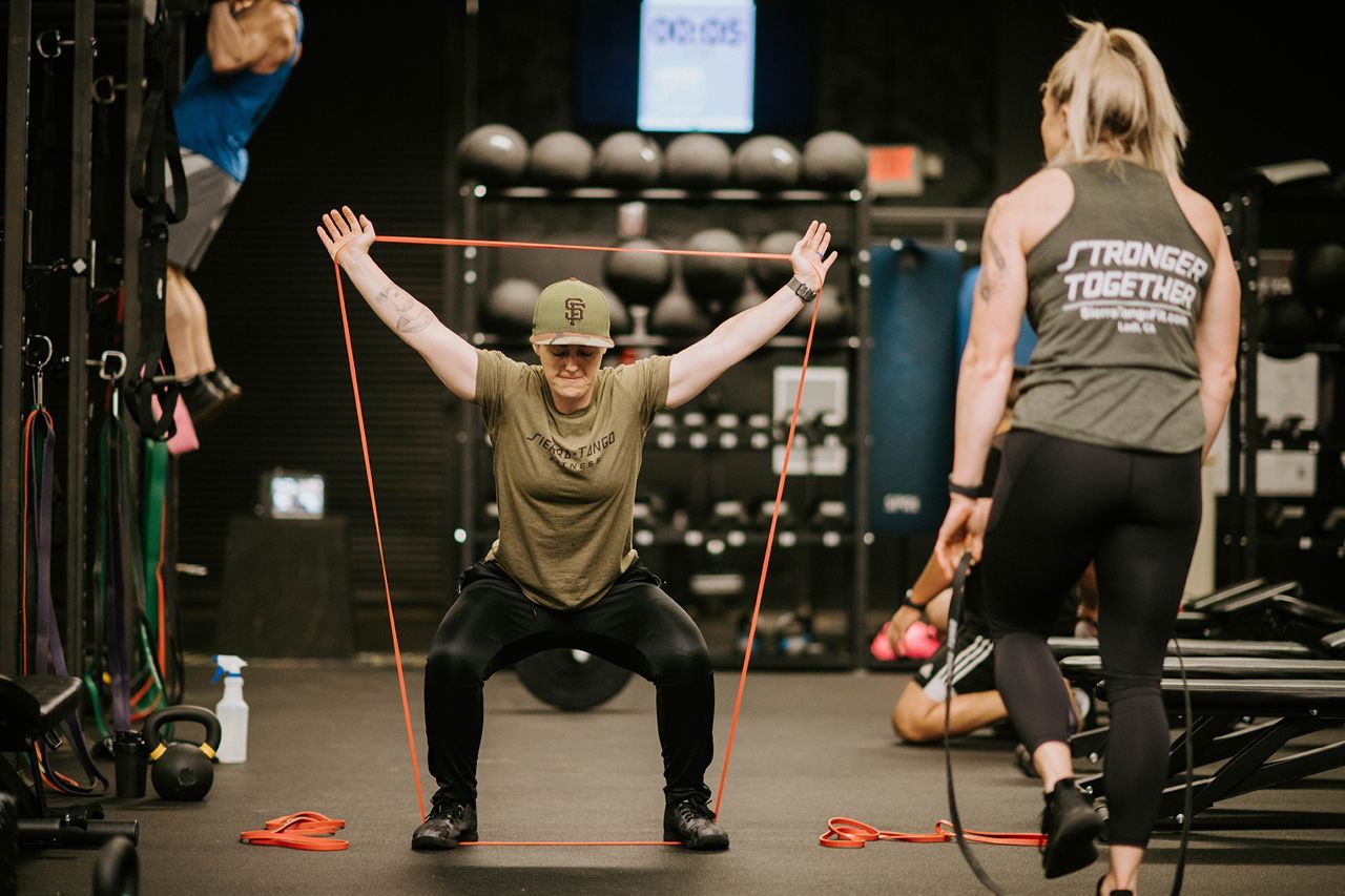 A woman is squatting with a resistance band in a gym.