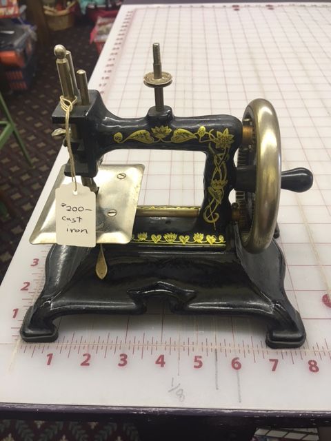 Antique black and gold sewing machine with gold floral details on a white grid, with a price tag.