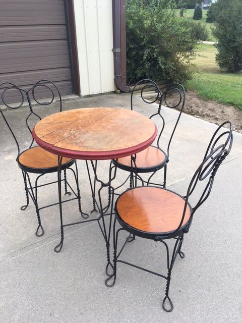 A vintage bistro set, including a round table and three chairs, made of black wrought iron with wooden seats and tabletop.