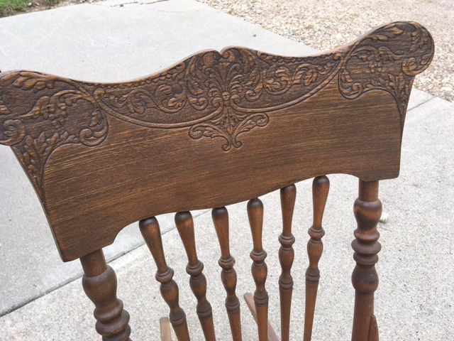 Wooden rocking chair back with ornate carvings and turned spindles.
