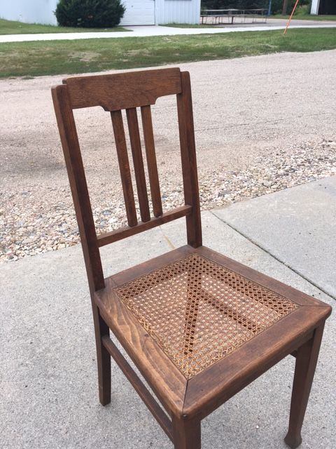 Wooden chair with woven seat, three back slats, on a concrete surface.