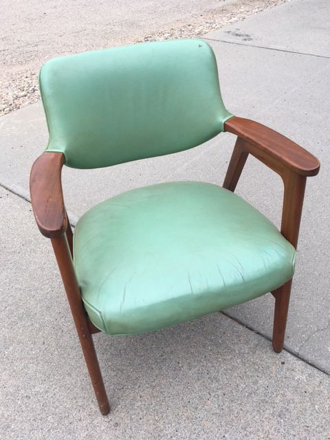 Green mid-century modern chair with wood arms and legs, on a concrete surface.