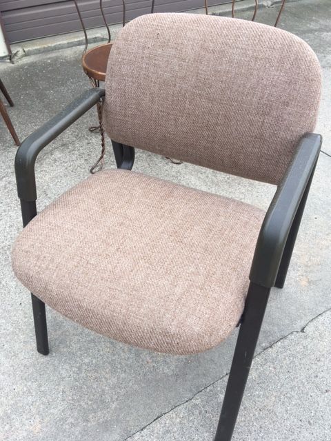 Brown upholstered office chair with black arms and legs, set outside on concrete.