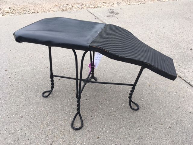 Black wrought iron bench with a padded seat, outdoors on concrete.