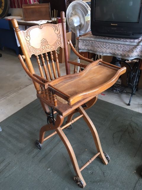 Wooden antique high chair with a tray, rolling wheels, and ornate back.