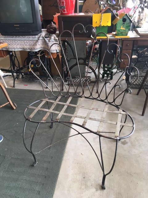 Black wrought-iron outdoor chair with lattice seat, against a cluttered background.