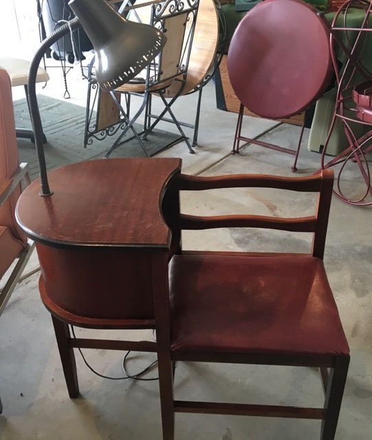 Side table with built-in chair, dark wood with a lamp. Chair has burgundy seat, various outdoor furniture in background.