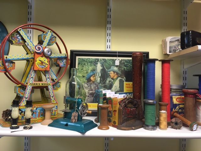 Shelf with antique toys, including a Ferris wheel, sewing machine, spools of thread, and framed print.