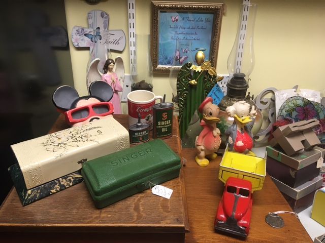 Antique shop display: Mickey Mouse ears glasses, Singer boxes, Campbell's cans, Donald Duck figures, a red toy car.