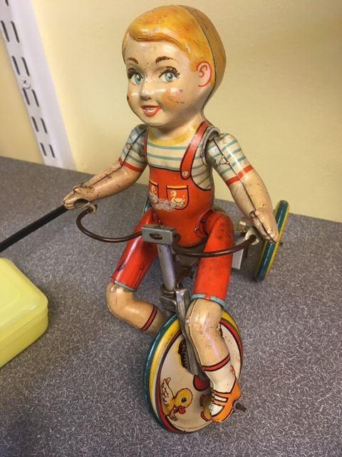 Vintage wind-up toy of a boy on a unicycle; he is in red overalls and smiling.