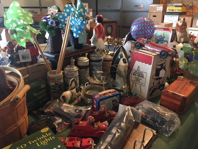 Table with assorted antique items, including steins, toys, figurines, and decorations for sale.