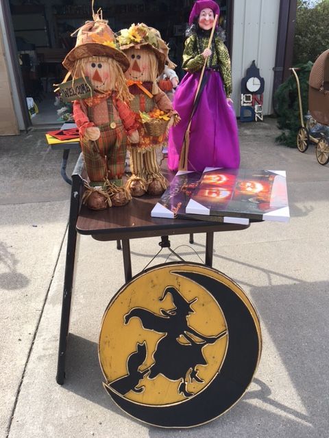 Halloween decorations for sale: scarecrows, a witch figure, and a witch and cat sign.