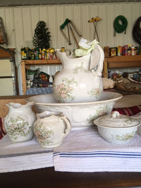 A vintage porcelain washbasin set with floral patterns, set on a white cloth.