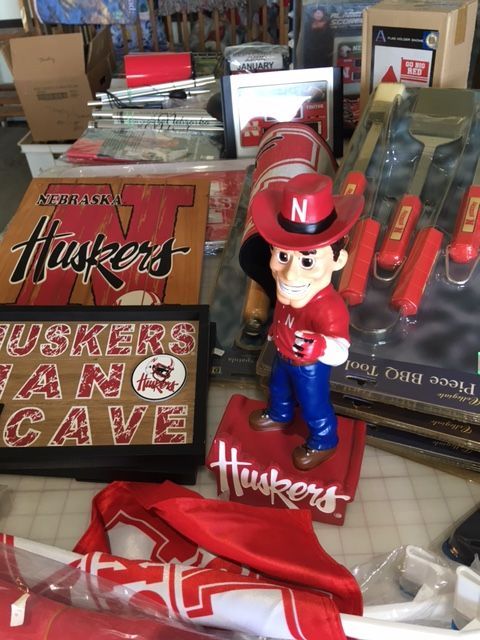 Nebraska Huskers fan items: signs, bobblehead, barbecue tools, red and white clothing.